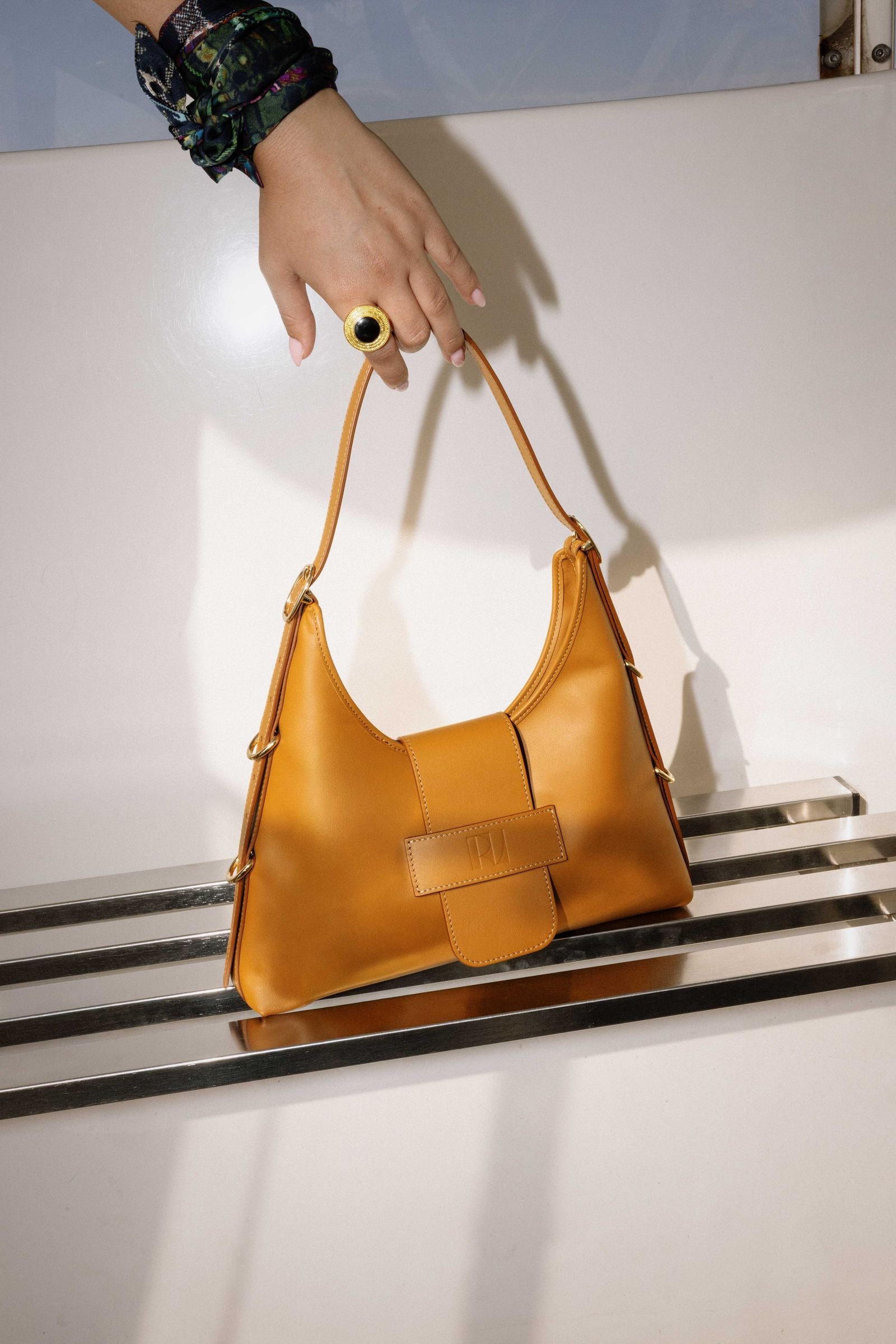 une main attrape le sac fada taille M camel posé sur un banc-la bague pepite spartiate est mis à l'index