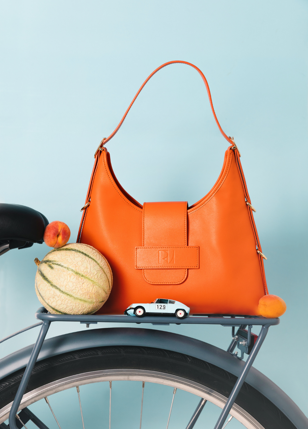 le sac fada taille M orange est posé sur un porte bagage de vélo avec un melon et des abricots