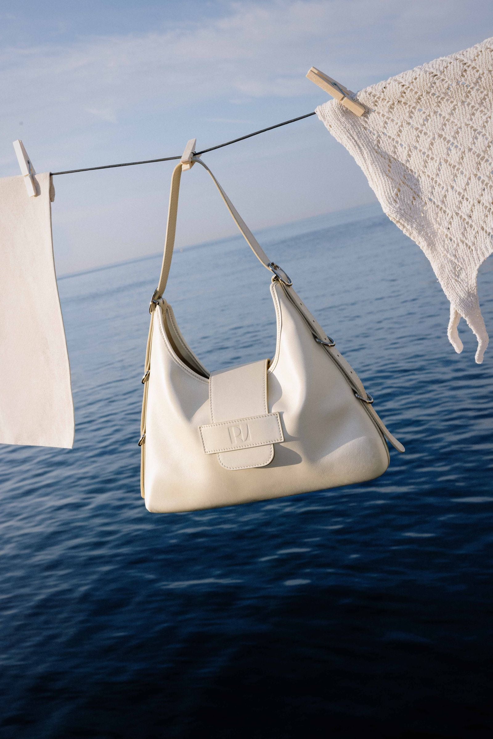 le sac fada taille M jaune pâle est mis scène sur un fil à linge avec d'autres vêtements qui sèchent face à la mer
