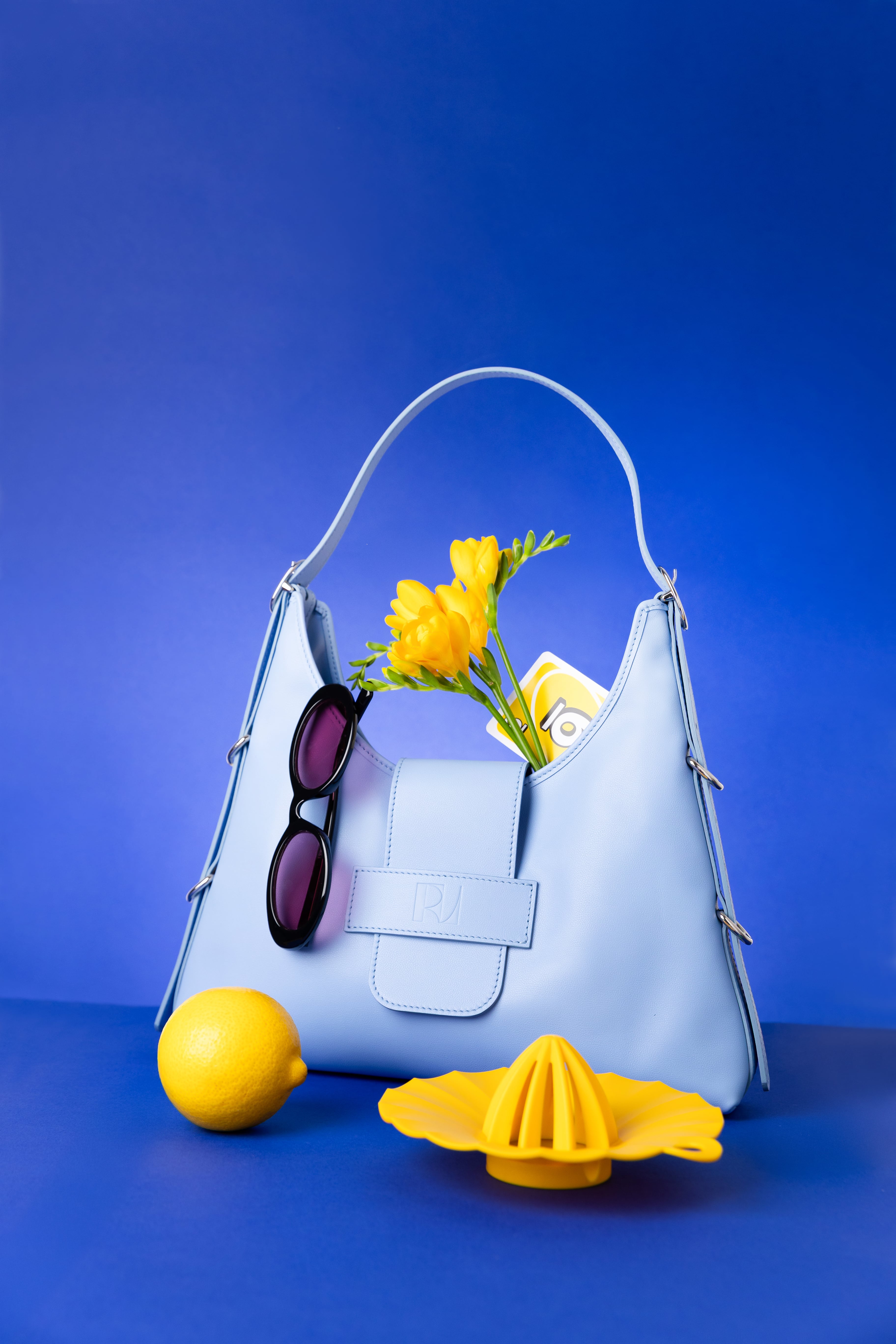 sac fada taille M bleu clair posé sur une table bleue indigo avec des élements jaune autour. un bouquet de jonquilles dans le sac